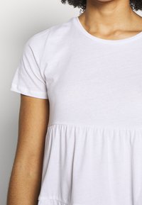 Bílé tričko s krátkým rukávem vyrobené z bavlny, s přiléhavým korzetem a nařaseným peplum lemem, s jemnou texturou a kulatým výstřihem.