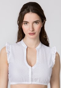 White short-sleeve blouse featuring a deep v-neck, frill detailing on shoulders, and eyelet fabric with small perforations. Elasticized hem.