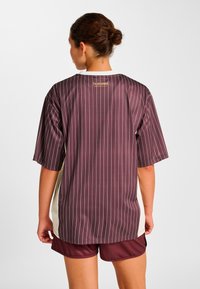 Bordeauxrød sportstrøje med hvide lodrette striber, korte ærmer og et kontrastfuldt lyst sidepanel; har en gylden logo på bagsiden af halsudskæringen.