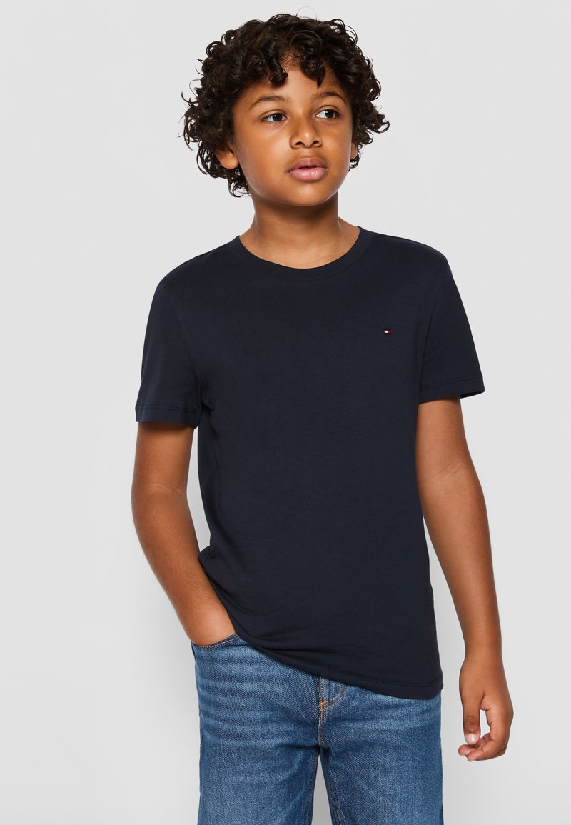 T-shirt di cotone blu navy con collo rotondo, maniche corte e un piccolo dettaglio del logo sul petto. Indossato con jeans di denim blu.