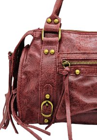 Sac en cuir texturé rouge avec quincaillerie dorée, comportant des fermetures éclair, une bandoulière détachable et des pompons décoratifs sur le côté.