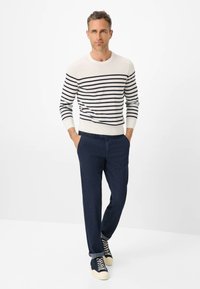 Maglione a righe in crema e blu navy, abbinato a pantaloni blu scuro e sneakers azzurre. Il maglione presenta polsini e orlo a coste.