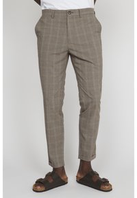 Bruna rutiga byxor i ett lätt material med smal passform, veckad front och uppvikta benslut, samt mörkbruna sandaler med öppna tår.