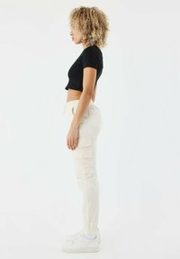 Schwarzes, kurzes T-Shirt und cremefarbene Cargo-Hosen mit elastischen Bündchen, die seitliche Taschen und einen lässigen Schnitt aufweisen. Weiße Sneakers runden den Look ab.