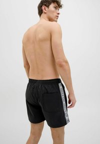 Zwarte zwembroek van lichtgewicht stof, met een elastische tailleband, zijzak en contrasterende logostreep langs de zijkant.