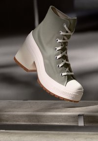 Zapato alto de lona verde claro con puntera de goma blanca y tacón grueso beige. Presenta cordones planos y suela texturizada para mayor agarre.