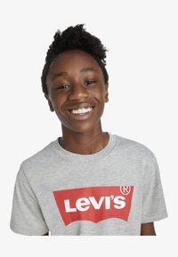Camiseta gris de manga corta con un destacado logo rojo de Levi's en el centro, fabricada en algodón con una textura suave.