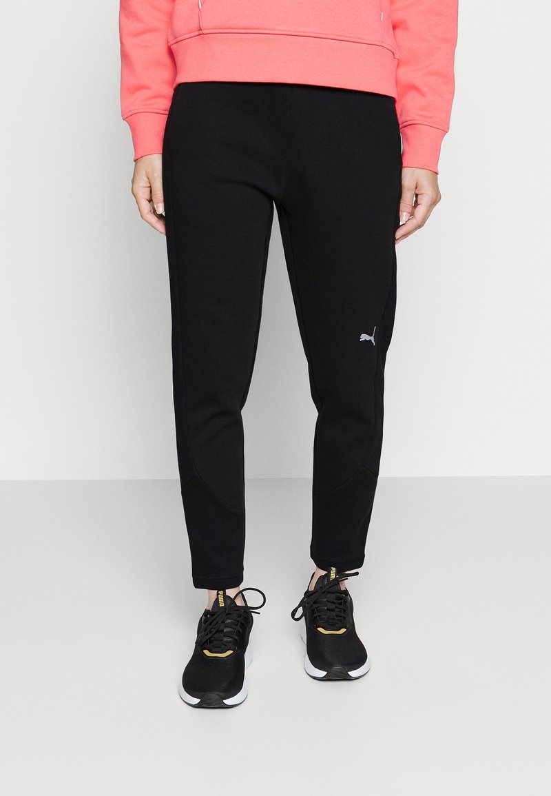 Schwarze Sweatpants mit taillierter Passform, aus weichem Stoff, mit einem silbernen Puma-Logo am linken Bein, kombiniert mit schwarzen Sneakern.