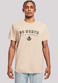 Beige cotton t-shirt with short sleeves featuring black text "GO NORTH" and an anchor logo. Classic crew neck design.