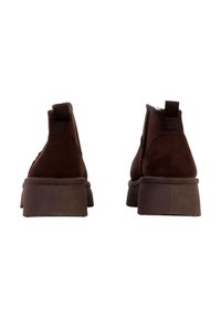 Bottines en daim marron avec une semelle basse et épaisse, dotées de languettes à l'arrière et de courbes lisses sur la partie supérieure.