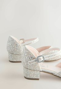 Brokatowe srebrne buty na niskim, klockowym obcasie, z miękkim różowym wnętrzem, ozdobnym paskiem i biżuteryjnym akcentem na pasku.