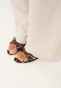 Sandalice s leopard uzorkom i crnim detaljima, s preklopnim trakama, u kombinaciji s bež širokim hlačama, ističu nožne prste.