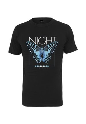 Homme debout portant un T-shirt noir avec un papillon bleu et le texte « NIGHT », pantalon vert olive et baskets montantes bleu clair.