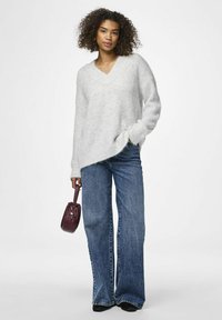 Šviesiai pilkas per didelis megztinis su V formos iškirpte, derinamas su mėlynomis plačiomis džinsinėmis kelnėmis. Modelis laiko mažą bordo spalvos rankinę. Matoma minkšta tekstūra.