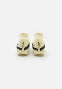 Botas de fútbol amarillas con un diseño similar a un calcetín, que presentan una franja negra y una marca en el talón. Material superior suave, tacos moldeados.