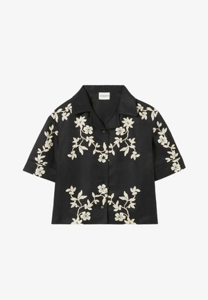 Chemise noire à manches courtes avec broderie florale blanche, col chemise et ouverture boutonnée à l'avant. Texture lisse et coupe décontractée.
