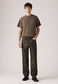 Olivnozeleno bombažno majico s kratkimi rokavi, v kombinaciji s temnozelenimi ravnimi hlačami. Obuta z črnimi čevlji, kar ustvarja sproščen videz.