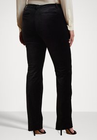 Pantaloni negri din catifea cu un design drept, având buzunare la spate și o textură netedă, asortați cu sandale negre cu toc înalt.