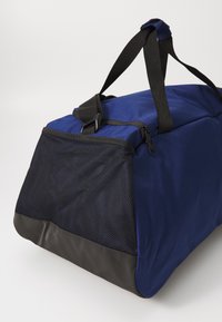 Sinine duffle-kott tekstureeritud viimistlusega, musta võrkpaneeliga ja plastaktsentidega. Omab kaht kät ja lukuga sulgemist.