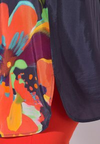 Tissu floral multicolore vif avec des pétales orange, verts et violets audacieux à côté d'un tissu uni bleu marine foncé, montrant un détail de vêtement.
