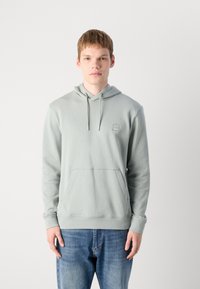 Lichtgroene hoodie met een voorzak, een capuchon met trekkoord en een klein logo-opdruk. De stof lijkt zacht en glad; de manchetten en onderrand zijn rib gebreid.