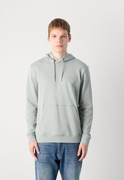 Hoodie vert clair avec une poche avant, un capuchon à cordon de serrage et un petit patch logo. Le tissu semble doux et lisse ; les poignets et l'ourlet sont côtelés.