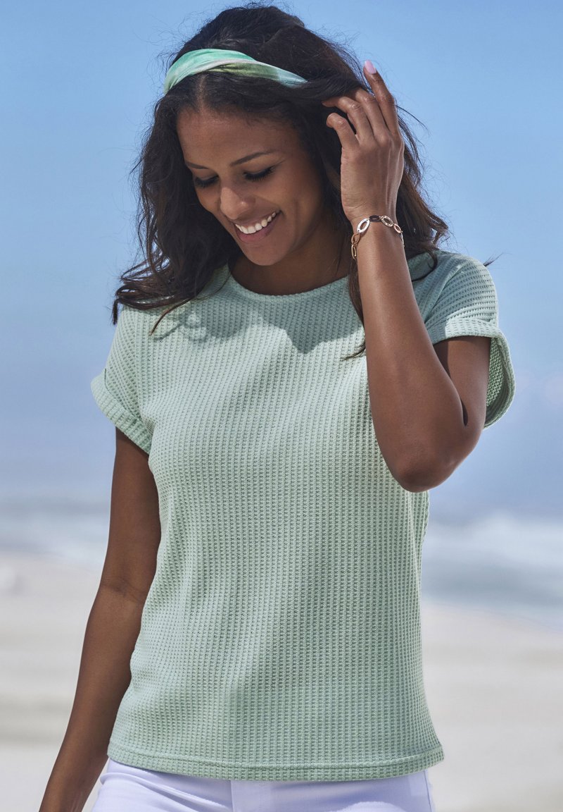 Svetlozelené textúrované pletené tričko s krátkymi rukávmi a okrúhlym výstrihom, spárované s bielymi nohavicami. Súčasťou sú vzorovaný čelenka a náramok.