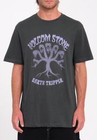 Tummanharmaa puuvillapaita, jossa on violetti graafinen kuvio puusta, jossa on käärmeennäköisiä päitä, sekä teksti "VOLCOM STONE EARTH TRIPPER". Lyhyet hihat.