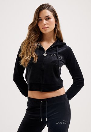 Black velour cropped hoodie with zipper, front pocket, and "JUICY" logo. Paired with matching black pants featuring a drawstring and logo.