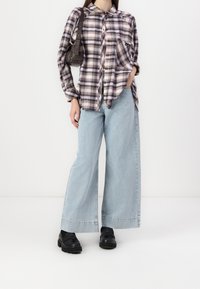 Ruudullinen flanellipaita ruskean ja kerman sävyissä, yhdistettynä leveälahkeisiin vaaleansinisiin farkkuihin ja mustiin korkokenkiin. Sisältää pienen mustan käsilaukun.