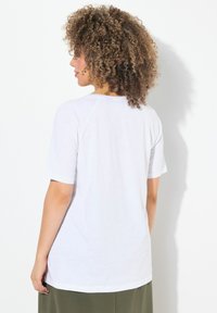 Camiseta blanca de manga corta con un ajuste relajado, con un cuello redondo y una tela suave y ligera. La vista posterior muestra detalles de costura.