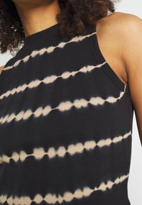 Haut noir sans manches avec une texture côtelée, présentant un motif tie-dye de rayures horizontales beige et blanches alternées.