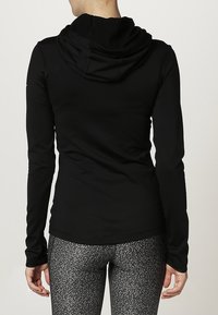 Sudadera negra de manga larga con capucha estructurada, hecha de un material suave, combinada con leggings grises estampados que presentan un diseño abstracto sutil.