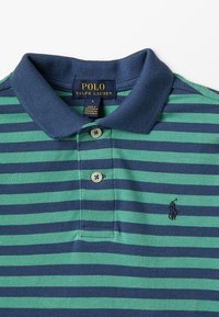 Marinblå och grön randig polotröja med krage, försedd med tre knappar och en liten broderad logotyp på vänster bröst.