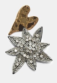 Metallisk broche med et gyldent, hamret hjerte og et sølvfarvet blomstermotiv, udsmykket med klare rhinsten og metalliske frøperler.