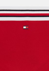 Rød bomulds skjorte med hvide og sorte vandrette striber på kraven, forsynet med et lille logo patch i blå, hvid og rød.