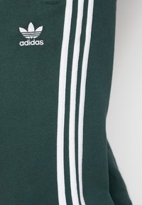 Mörkgrön Adidas-kontaktsmaterial med vita tre ränder och broderad Adidas treklöverlogotyp.