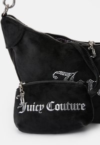 Črna nubuk torbica z srebrnimi dodatki, z zadrgo in manjšim žepkom, ki nosi napis "Juicy Couture" v kovinskem tisku.