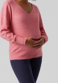 Weicher rosa Pullover in lockerer Passform, mit V-Ausschnitt und gerippten Bündchen, kombiniert mit dunklen Leggings. Die Textur wirkt kuschelig und warm.