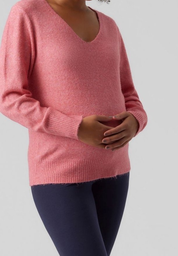 Weicher rosa Pullover in lockerer Passform, mit V-Ausschnitt und gerippten Bündchen, kombiniert mit dunklen Leggings. Die Textur wirkt kuschelig und warm.