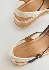 Sandalo espadrille in pelle marrone chiaro con piattaforma in juta intrecciata e cinturini blu navy. Presenta una soletta testurizzata impressa con la dicitura "NEXT FOREVER COMFORT."