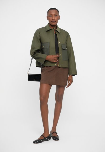 Olive green jacket with two front pockets, paired with a brown skirt and black flats. The jacket features a zip closure and gold hardware.
