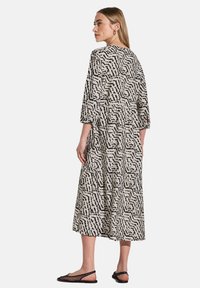 Schwarz-weiß gemustertes Maxikleid mit einem fließenden Design, Dreiviertelärmel und gestuftem Saum. Hergestellt aus leichtem Stoff.