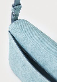 Light blue denim bag with a textured surface and smooth leather strap. Features a simple, modern shape and minimalistic design.