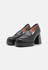 Black leather platform loafers with a rounded toe, wide strap detail, and tall block heel. Smooth texture and stitched accents on the upper.