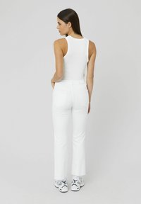 Un haut blanc sans manches associé à un jean flare blanc. L'ensemble présente un design ajusté et une texture lisse, rehaussé par des baskets décontractées.