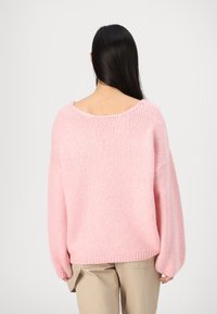 Maglione over-size di un morbido rosa con un ampio scollo e lunghe maniche voluminose. Tessuto lavorato a maglia, orlo a costine e vestibilità casual. Abbinato a pantaloni beige.