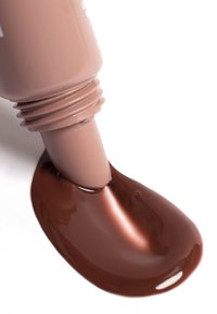 Creamy brown liquid makeup oozing from a light brown tube, with a textured finish, on a white background, showcasing smooth consistency.