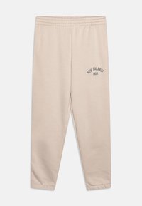 Béžové tepláky vyrobené z měkké tkaniny, s elastickým pasem a potiskem "New Balance 1906" v tmavě šedé barvě na levé noze.