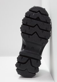 Semelle de chaussure en caoutchouc noir avec des crampons profonds en zigzag et horizontaux, taille 37, photographiée sur un fond blanc en angle.